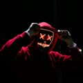 A spooky illuminated mask figure with a red hoodie in a dark setting, perfect for Halloween themes.